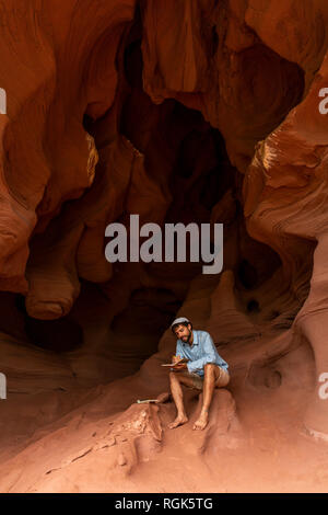 Young man sitting in a cave, taking notes Stock Photo