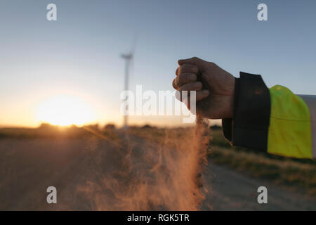 Close-up of man's hand scattering soil at a wind turbine at sunset Stock Photo