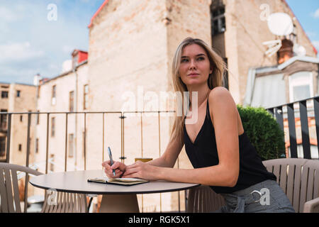 Portrait of young woman sitting on balcony taking notes Stock Photo