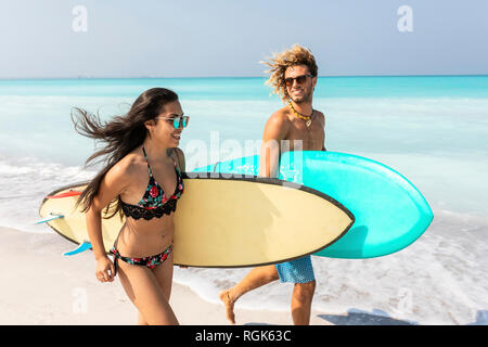 Couple running on the beach, carrying surfboards Stock Photo