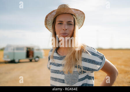 Portrait of young woman at camper van in rural landscape sticking out her tongue Stock Photo