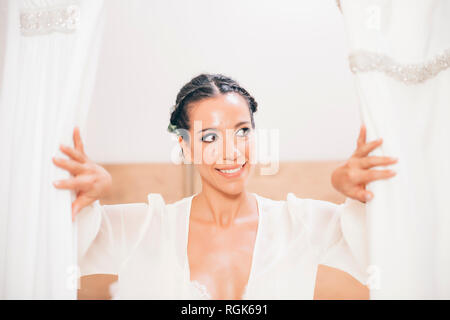 Smiling woman opening curtain looking sideways Stock Photo