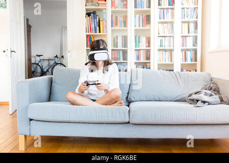 Girl sitting on the couch at home using Virtual Reality Glasses Stock Photo