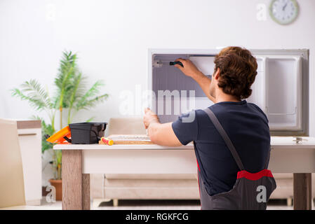 Young handsome contractor repairing fridge Stock Photo