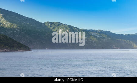Beautiful coast of Haiti just after sunrise. Morning haze on lush green mountains rising from the calm Caribbean. Peaceful vacation paradise. Stock Photo