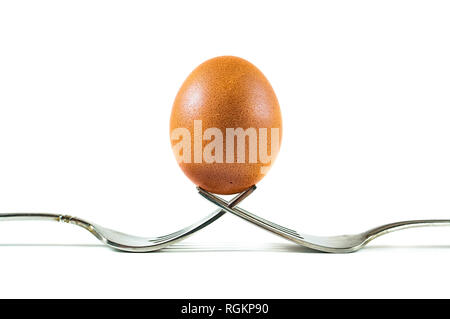 A brown organic egg balanced on two forks isolated on a white background. Stock Photo