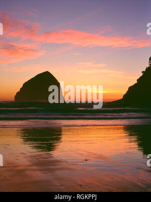 USA, Oregon, Cape Kiwanda State Park, Haystack Rock and Cape Kiwanda are silhouetted by sunset afterglow. Stock Photo