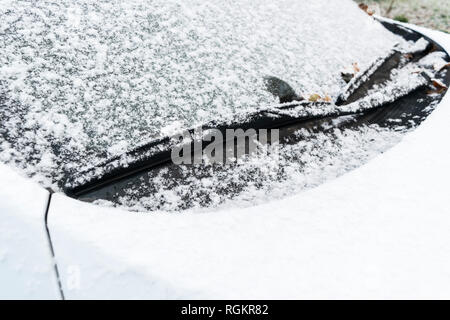 Snow covered car window with wipers, macro, close up. Car wiper blades clean snow from car windows. Flakes of snow covered the car. Stock Photo