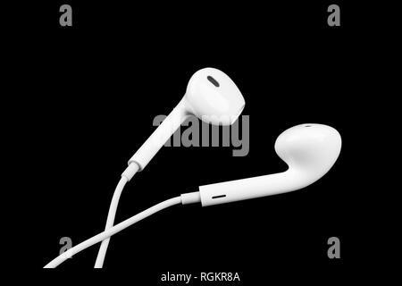 White little headphones isolated on black background. Earphones isolated on black background. Stock Photo