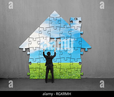 Businessman assembling house shape puzzles with beautiful landscape on concrete wall Stock Photo