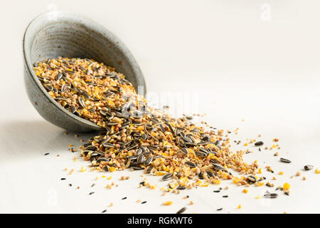 bird food from mixed seeds like sunflower, corn, millet and more, are falling out of a bowl on a light background, copy space, selected focus, narrow  Stock Photo