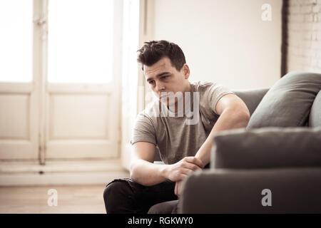 Portrait of young man felling depressed and desperate crying alone in sofa home suffering emotional pain and unhappiness. In People Broken heart, Bull Stock Photo