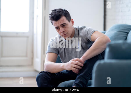 Portrait of young man felling depressed and desperate crying alone in sofa home suffering emotional pain and unhappiness. In People Broken heart, Bull Stock Photo