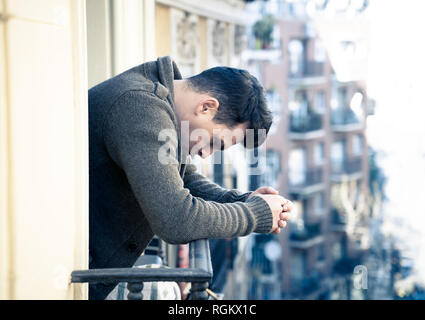 Sad unhappy depressed young man crying and suicidal feeling desperate, isolated and worthless staring down the street on home balcony In People Depres Stock Photo
