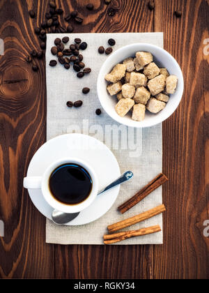 Cup of coffee, bowl with cane sugar, cinnamon sticks and coffee beans on the gray napkin on the wooden table. Top view Stock Photo
