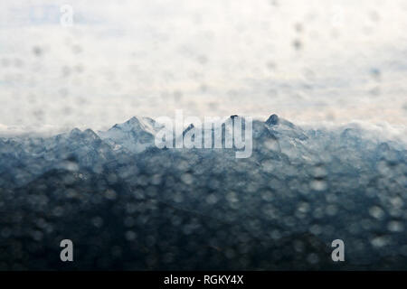 High contrast mountain glacier in south of France in summer, view through deliberately out of focus window, water drops and rain. Bright cloudy sky. Stock Photo