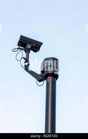 Black security camera high up on a pole against a sky background Stock Photo