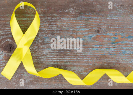 yellow ribbon-childhood cancer awareness symbol on the wooden background with copy space. Stock Photo