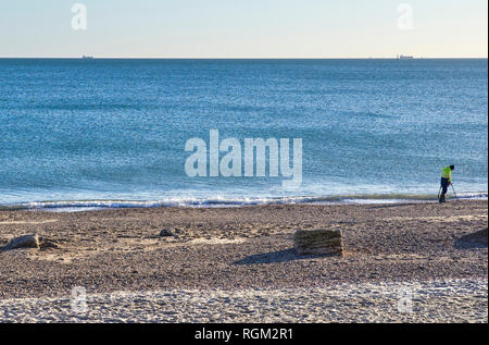 Eastney beach a lone man searches with a metal detector with cargo ships on the horizon Stock Photo