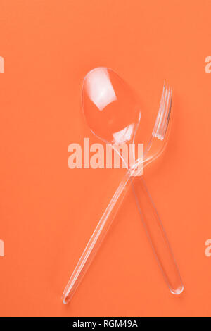 Transparent plastic fork and spoon on orange background top view Stock Photo