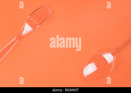 Transparent plastic fork and spoon on orange background top view with copy space Stock Photo