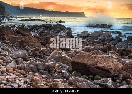 Bucks Mills, Devon, UK. 30th January 2019. After a cold overcast day in North Devon, the clouds finally part as the sun starts to set over the rocky shoreline at Bucks Mills. The seaspray from the incoming tide partially hides the distant white fishing village of Clovelly and Blackchurch Rock on the Hartland Peninsula. Credit: Terry Mathews/Alamy Live News Stock Photo