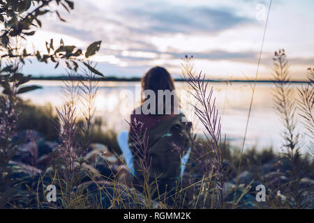 Young woman sitting at lake Inari, looking at view, Finland Stock Photo