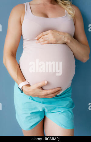 Mid-section of pregnant woman standing at blue wall Stock Photo