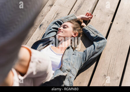 Relaxed young woman lying on wooden boards in sunshine Stock Photo