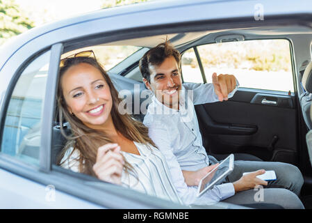 Smiling couple on back seat of a car looking out of window Stock Photo