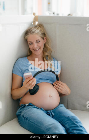 Pregnant woman holding headphones at her belly stock photo
