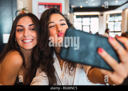 Portrait of two friends taking selfie with smartphone in a coffee shop having fun Stock Photo