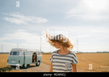 Blong young woman at camper van in rural landscape shaking her hair