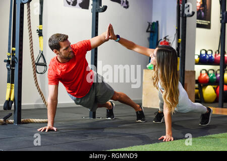 Couple exercising side plank with high-five in a gym Stock Photo