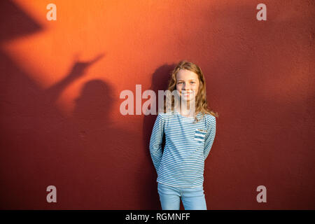 Portrait of smiling girl in front of a red wall with shadow Stock Photo