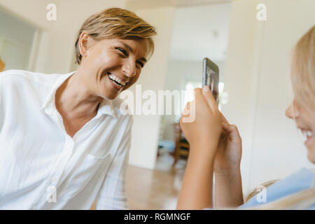 Daughter taking smartphone picture of happy mother Stock Photo