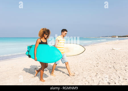 Couple walking on the beach, carrying surfboards Stock Photo
