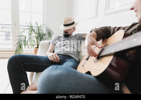 Relaxed couple sitting on couch, woman playing the guitar at home Stock Photo