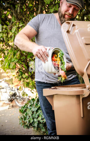 Mature man throwing kitchen scraps into bio-waste container Stock Photo