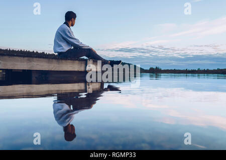 Young man sitting at lake Inari, looking at view, Finland