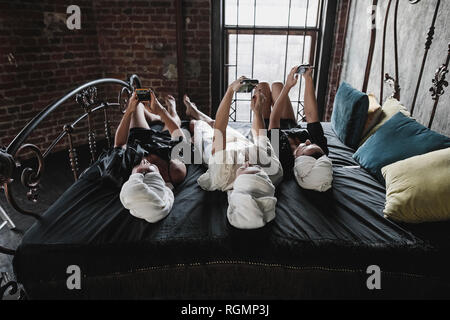 Three women with towels around her heads lying on bed taking selfies Stock Photo