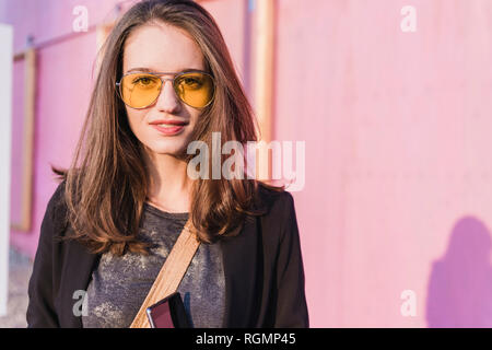 Portrait of smiling young woman wearing coloured sunglasses Stock Photo