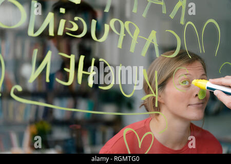 Portrait of young woman behind windowpane in a cafe with hand writing Stock Photo