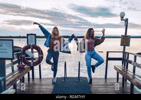 Two girl friends standing on one leg on a pier at Lake INari, Finland Stock Photo