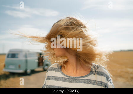 Blong young woman at camper van in rural landscape shaking her hair