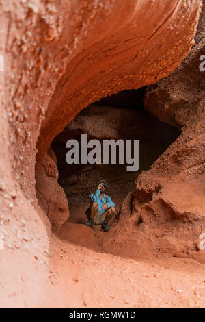 Young man sitting in a cave, looking through binoculars Stock Photo