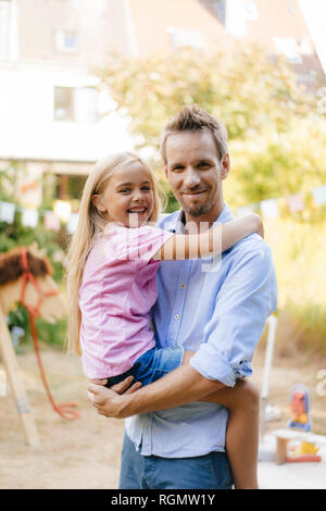 Portrait of smiling father carrying daughter in garden Stock Photo