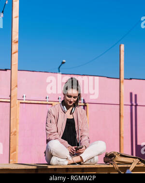 Young woman sitting on platform using cell phone Stock Photo