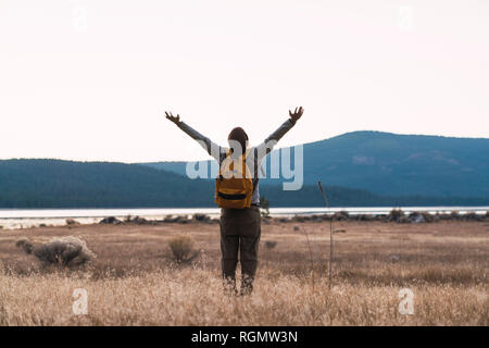 USA, North California, rear view of young man with raised arms on a hiking trip near Lassen Volcanic National Park Stock Photo