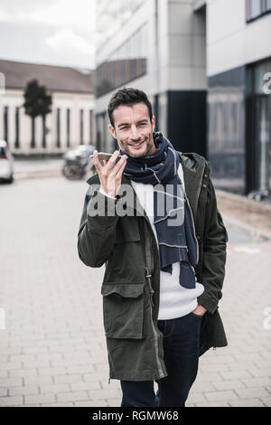 Mature man, wearing coat and scarf, walking in the city, talking on the phone Stock Photo